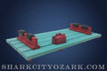 Model train tracks with red and black components on a wooden surface, featuring the website 'SHARKCITYOZARK.COM'.