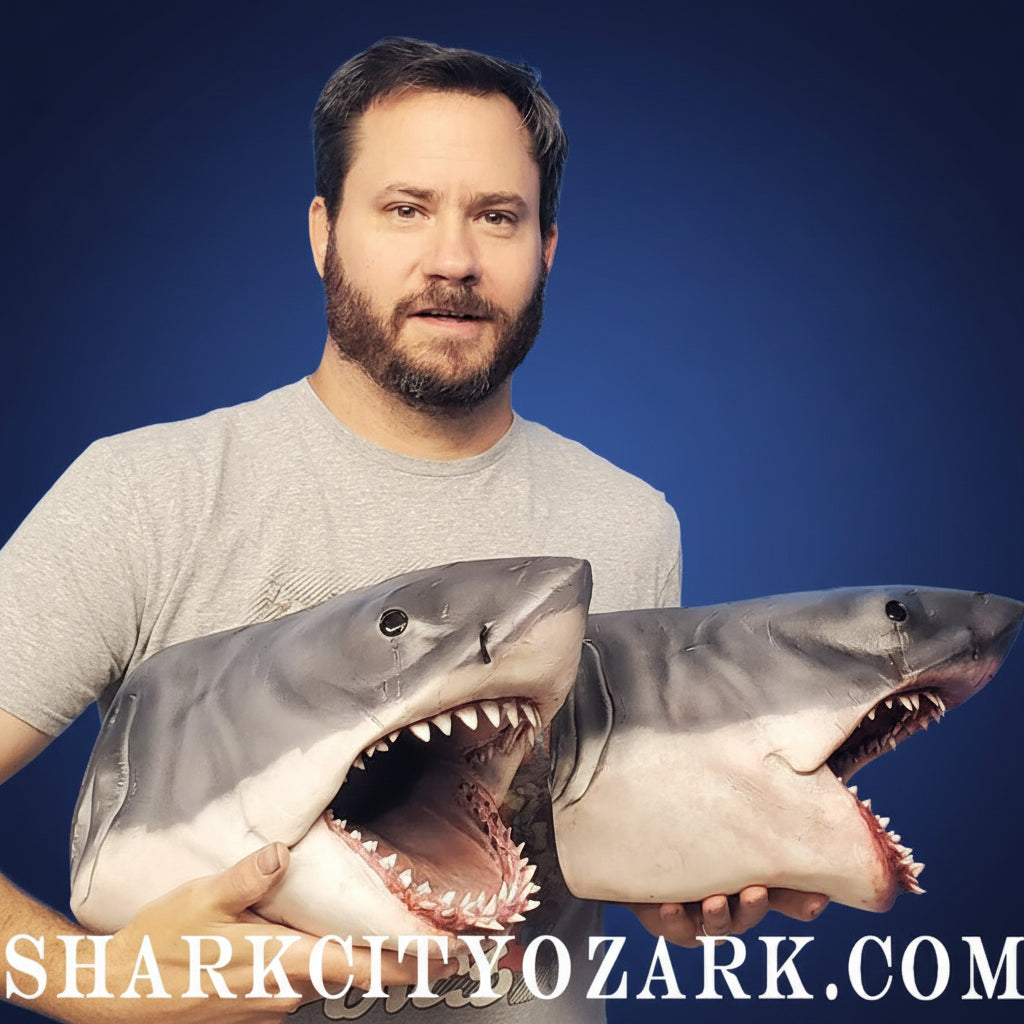Man holding two shark models against a blue background with 'Shark City Ozark' branding. jaws bruce shark
