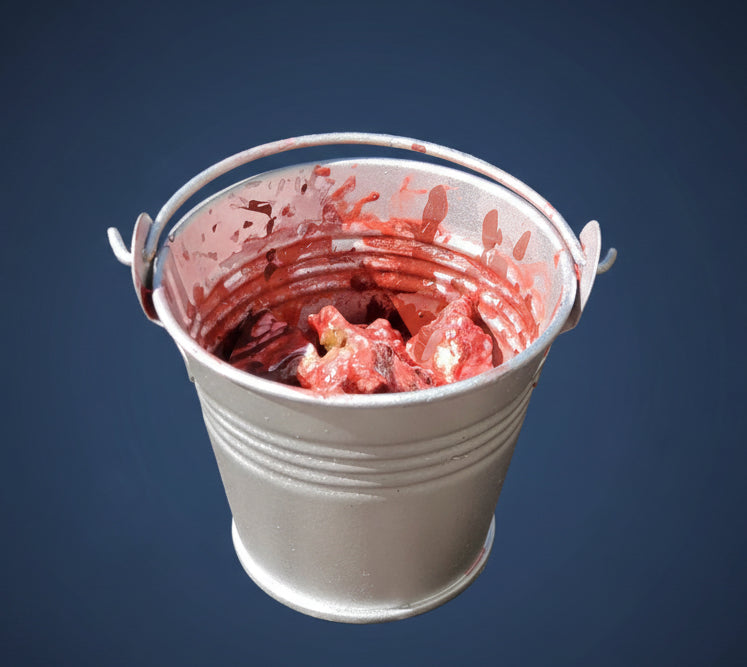 Metal bucket filled with red material on a wooden surface, with text about a scale chum bucket.